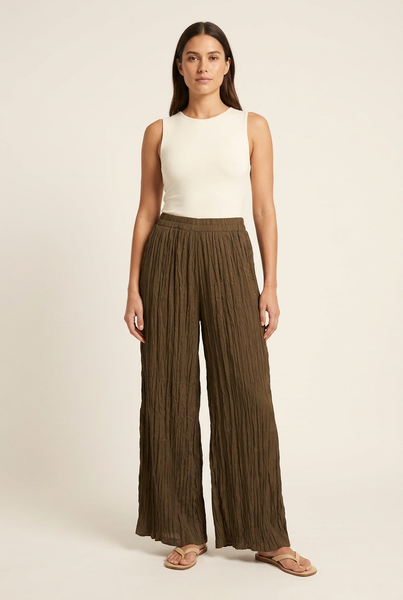 Model wearing brown crinkle-textured wide-leg trousers with an ivory top