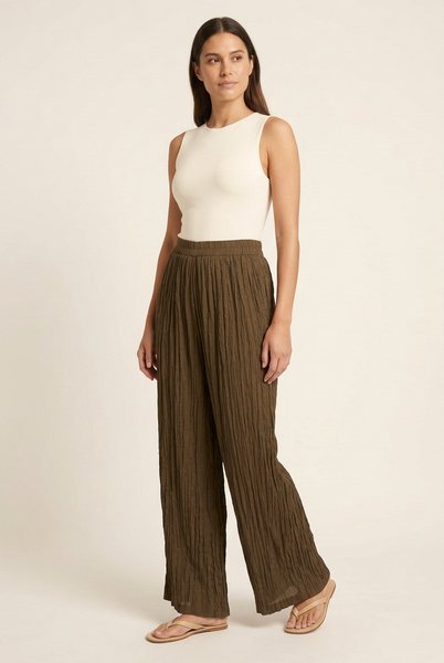 Model in a three-quarter pose wearing brown crinkle-textured wide-leg trousers and an ivory top