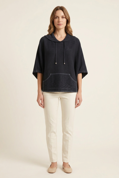 Full-body Western model wearing a black pleated cape top with ivory trousers and beige flats