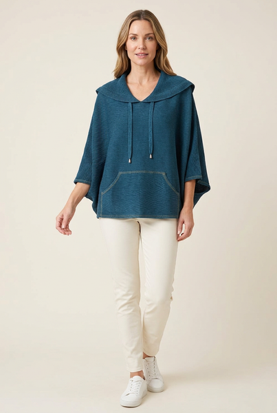 Model wearing a deep teal pleated drawstring cape top with ivory trousers