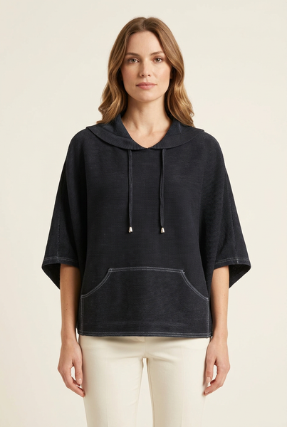 Western model wearing a black pleated drawstring cape top with contrast stitching and ivory trousers
